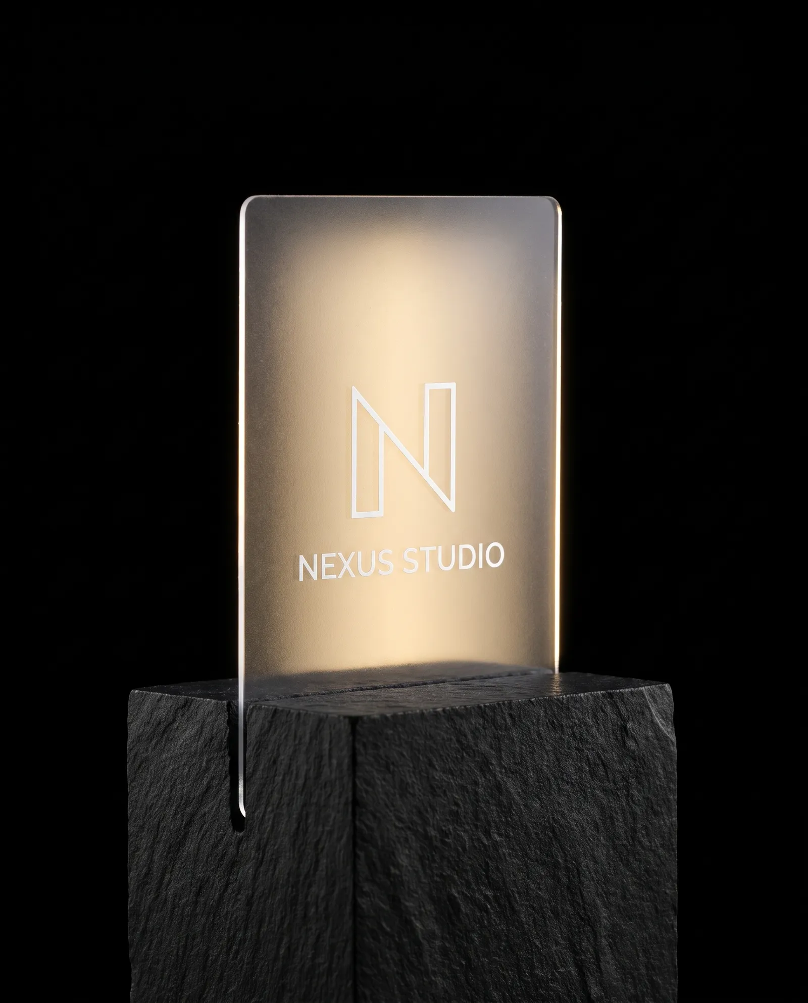 Clear plastic business card standing in a slot cut into black stone, lit from behind so the white printed logo glows.
