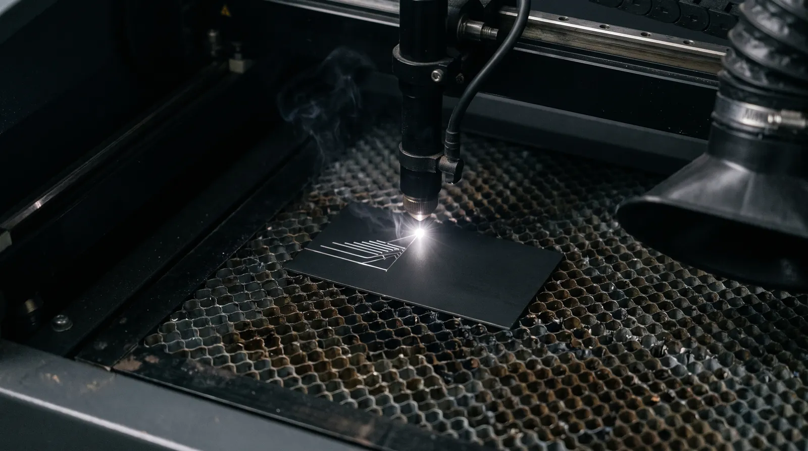 Fiber laser engraving a matte black metal business card on a honeycomb bed