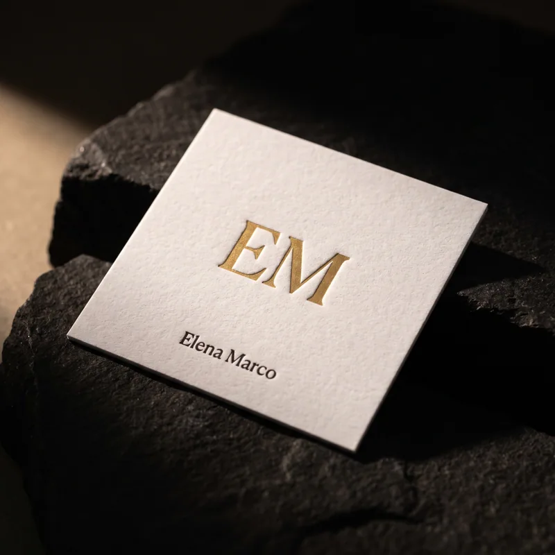 Square white cotton business card with matte gold foil EM monogram, Elena Marco