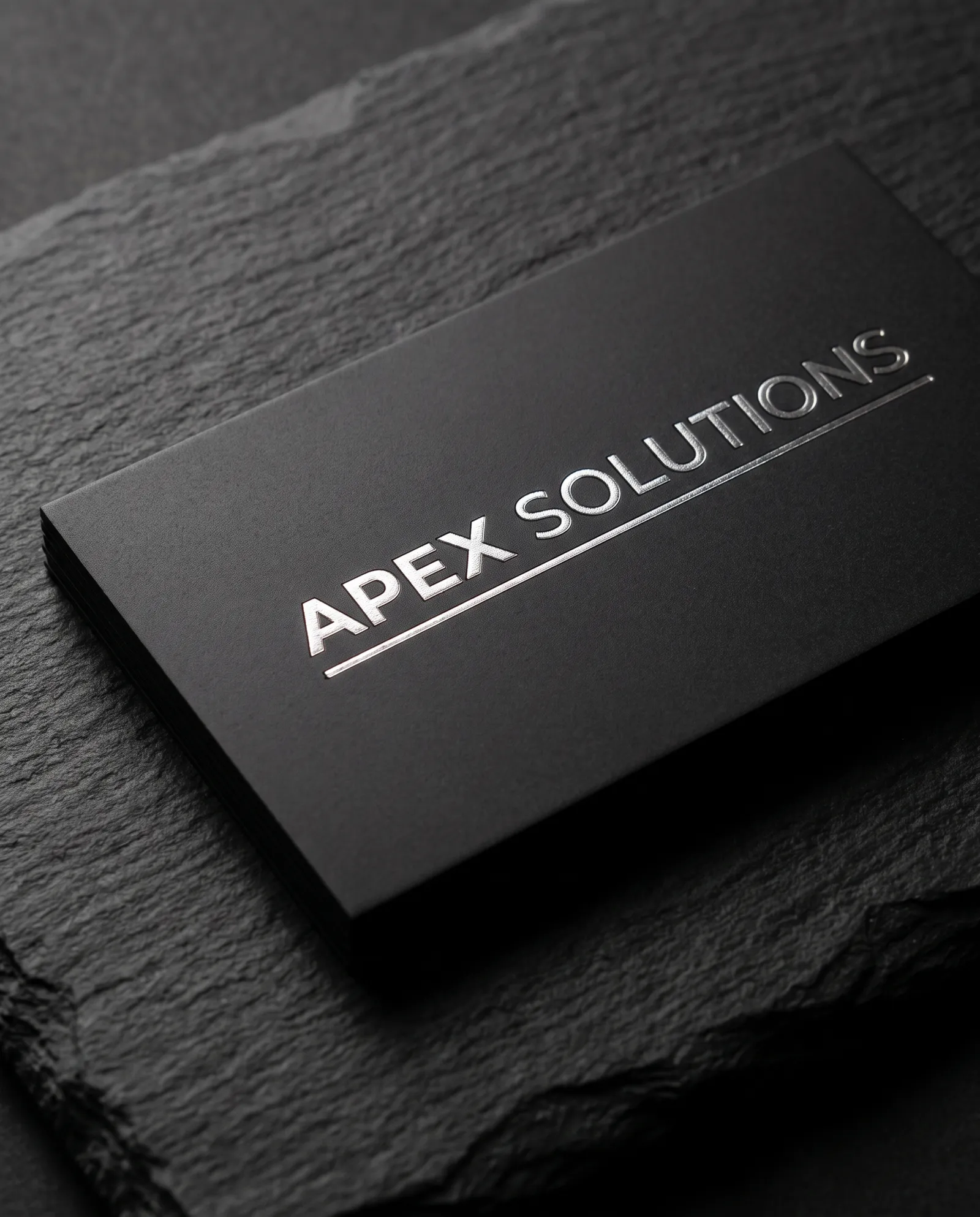 Macro of a black PVC business card with a silver foil wordmark, the foil edge sharp under a single soft light.