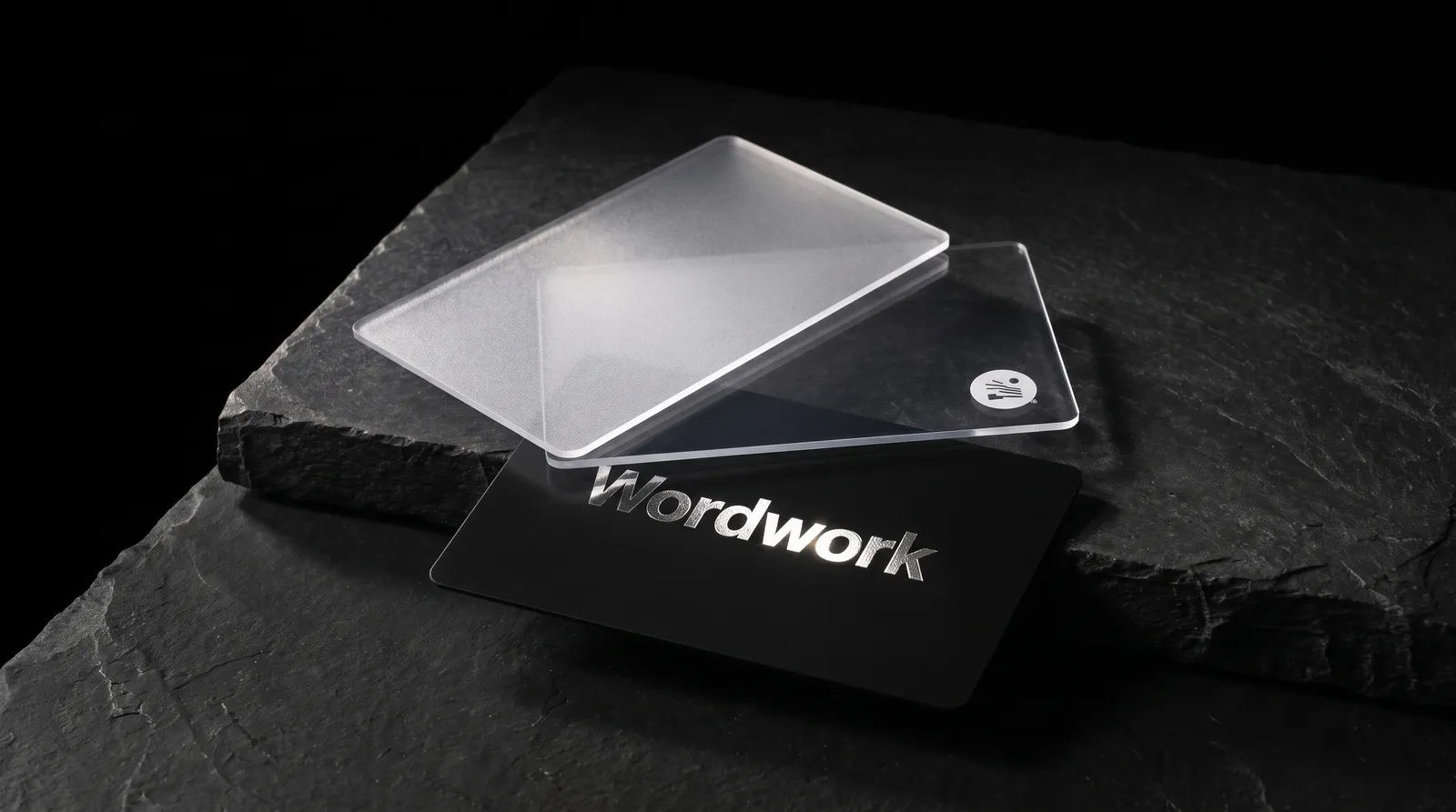 Frosted, clear and black PVC business cards fanned on a black slate plinth, the black card stamped in silver foil.